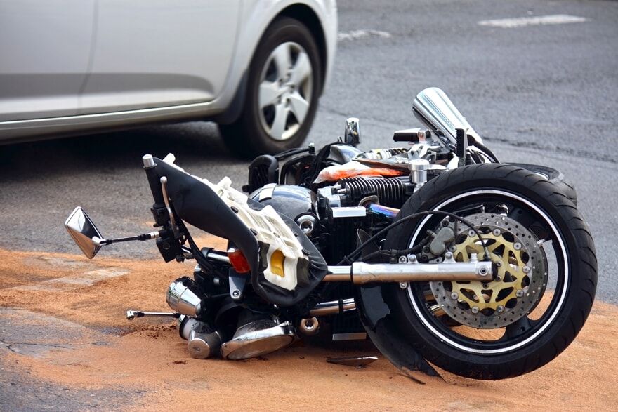 Motorcycle on the ground after being hit by a grey car